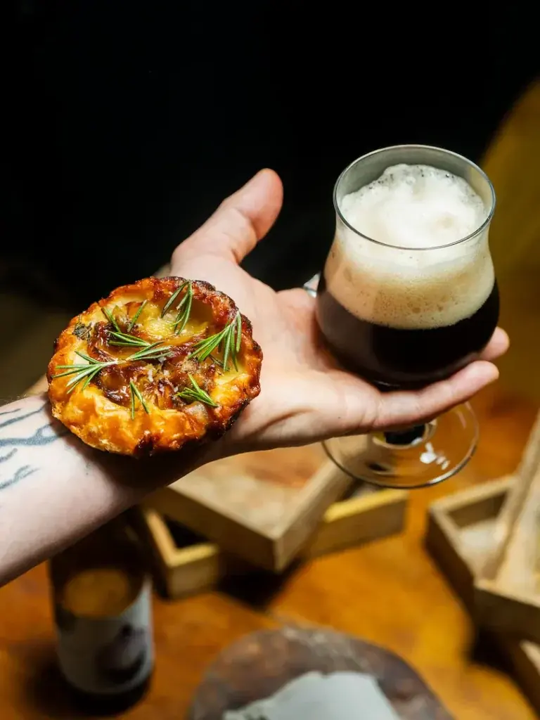 Une tartelette tenue à la main devant une bière brune.