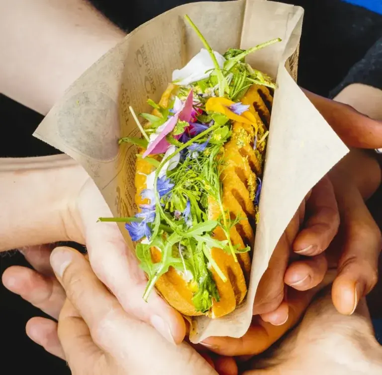 Des mains se passant un sandwich de street food.